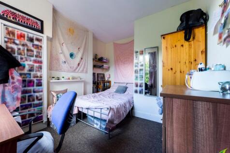 A cozy single bedroom featuring a bed, a desk w...