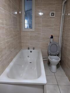 A clean bathroom featuring a bath and a toilet,...