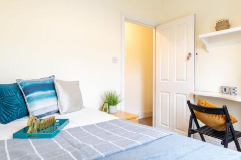 Bright, neatly styled bedroom with layered cush...