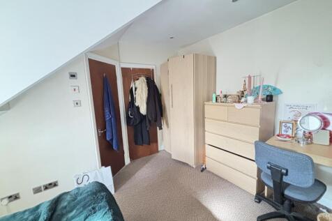 A well-lit bedroom featuring a bed, a desk with...