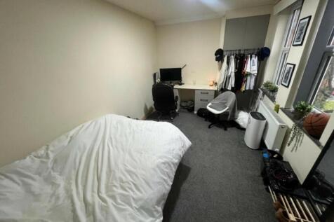 A cozy student bedroom featuring a simple bed s...