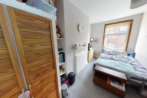 A cozy single bedroom featuring a bed, a window...