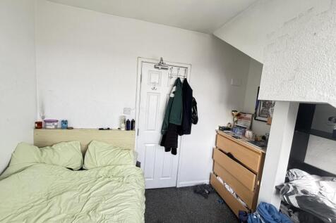 A modest bedroom with a bed, some clothing, and...