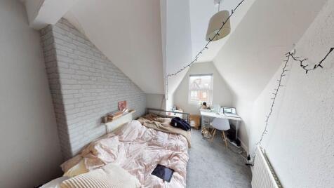 A cozy bedroom featuring a made bed with light-...