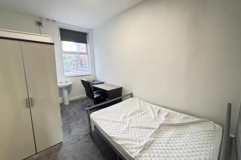 A tidy and well-lit student bedroom featuring a...