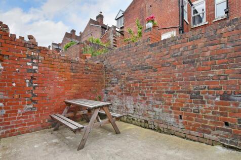 Enclosed paved rear yard with high red-brick wa...