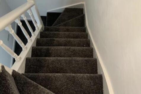 Carpeted internal staircase with white balustra...