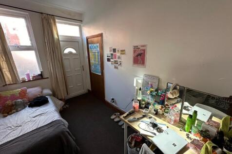 A modest bedroom with a bed, cluttered desk are...