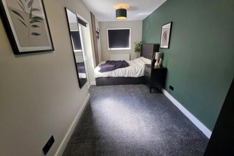 A stylish double bedroom featuring a dark green...