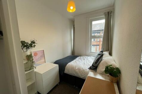 A cozy single bedroom with a tidy bed near a wi...