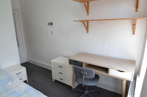 A cozy single bedroom featuring a simple desk a...