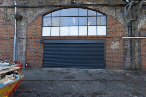 The front of an arch with a closed electric roller shutter entrance big enough for vehicle access, and separate pedestrian door.

