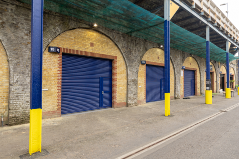 The front of an arch with a closed electric roller shutter entrance big enough for vehicle access, and separate pedestrian door.


