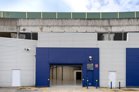 The front of a warehouse unit, with an open electric roller shutter entrance big enough for vehicle access, and a pedestrian door.