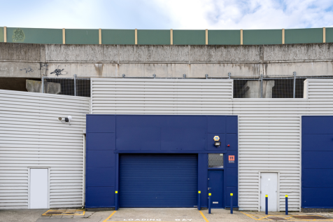 The front of a warehouse unit, with a closed electric roller shutter entrance big enough for vehicle access, and a pedestrian door.
