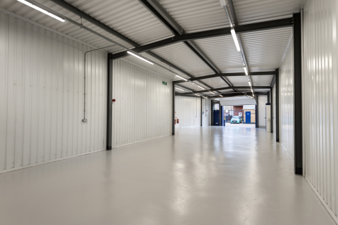 The interior of a warehouse unit, facing the front electric roller shutter, which is open and large enough for vehicle access.