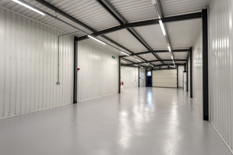 The interior of a warehouse unit, facing the front electric roller shutter, which is closed and large enough for vehicle access.
