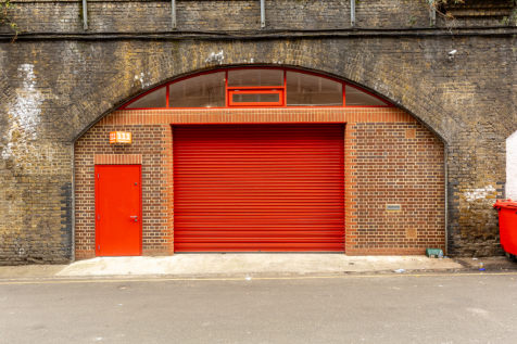 The front of an arch with a closed electric roller shutter entrance big enough for vehicle access, and separate pedestrian door.

