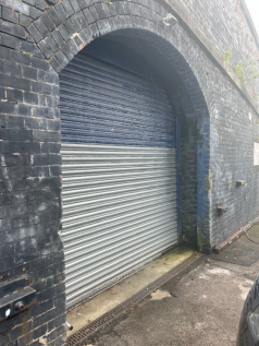 The front of an arch with a closed electric roller shutter entrance big enough for vehicle access.