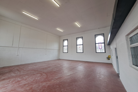 The interior of a warehouse unit, facing the front electric roller shutter, which is closed and large enough for vehicle access.