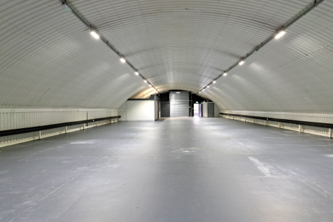 An empty arch with white lining, facing the front electric roller shutter entrance, which is closed. There is a WC cubicle at the front of the arch.