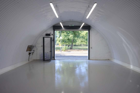 An empty arch with white lining, facing the front electric roller shutter entrance, which is open.