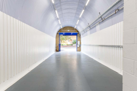 An empty arch with white lining, facing the front electric roller shutter entrance, which is open.