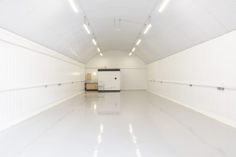 An empty arch with white lining, facing the front electric roller shutter entrance, which is open.