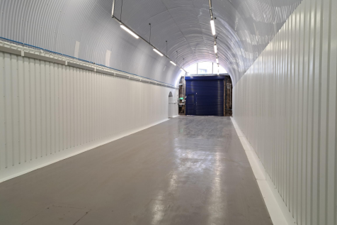 An empty arch with white lining, facing the front electric roller shutter entrance, which is closed.