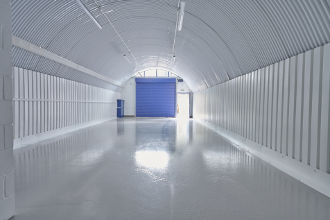 An empty arch with white lining, facing the front electric roller shutter entrance, which is closed.