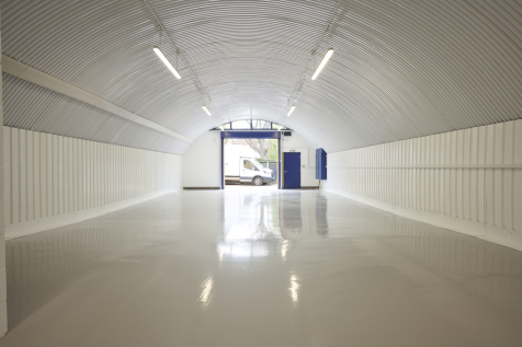 An empty arch with white lining, facing the front electric roller shutter entrance, which is open.