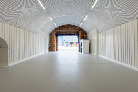 An empty arch with white lining, facing the front electric roller shutter entrance, which is open.