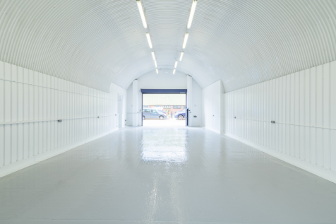 An empty arch with white lining, facing the front electric roller shutter entrance, which is open.