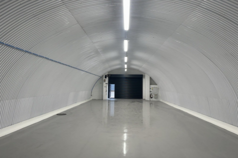 An empty arch with white lining, facing the front electric roller shutter entrance, which is closed.