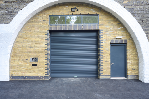 The front of an arch, with high level glazing, a closed electric roller shutter entrance big enough for vehicle access, and a pedestrian door.