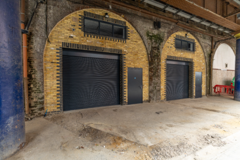 The front of an arch with a closed electric roller shutter entrance big enough for vehicle access, and separate pedestrian door.