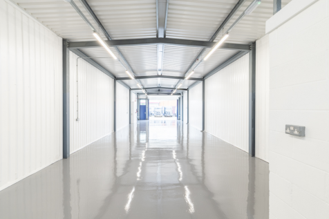 An empty arch with white lining, facing the front electric roller shutter entrance, which is open.