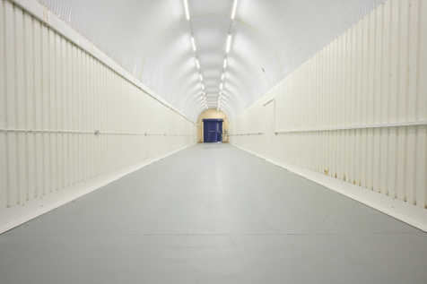An empty arch with white lining, facing the front electric roller shutter entrance, which is closed.