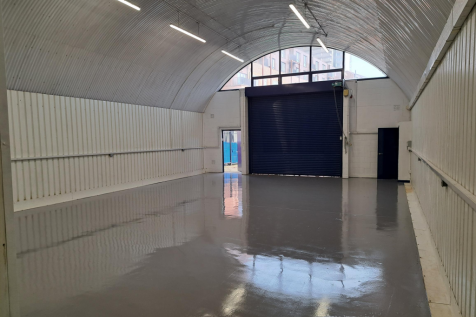 An empty arch with white lining, facing the front electric roller shutter entrance, which is closed.