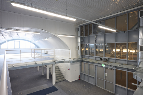 An arch with white lining and a ground floor level and a mezzanine level, connected by stairs.