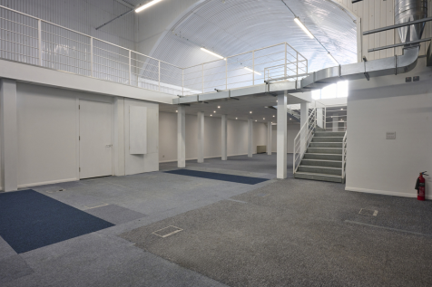 An arch with white lining and a ground floor level and a mezzanine level, connected by stairs.