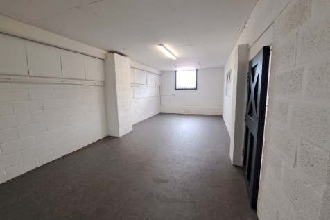 The interior of a warehouse unit, facing the front electric roller shutter, which is closed and large enough for vehicle access.