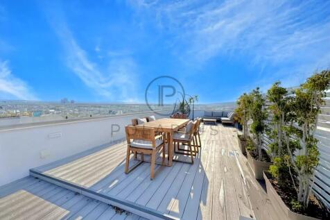 A rooftop deck with wooden furniture and potted pl
