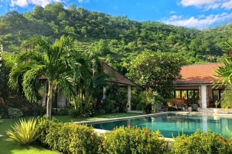 A tropical villa with a pool, surrounded by lush g
