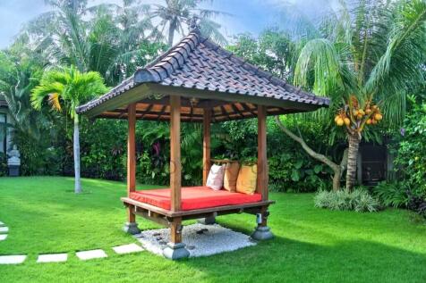 A tropical garden features a small wooden gazebo w