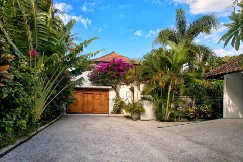 A tropical driveway leads to a wooden gate, surrou