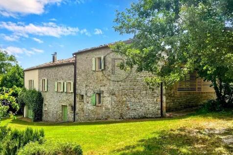 A rustic stone house with green shutters is surrou