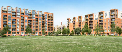 Modern orange-brick apartment buildings with balconies, set behind a grassy park with trees under a