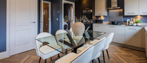 Modern kitchen with beige cabinets, black accents, dining table with six cream chairs, and a decorat