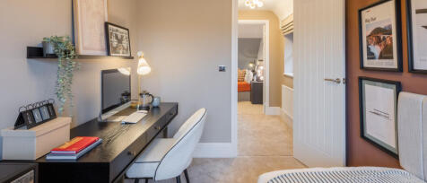 A cosy upstairs home office with a black desk, white chair, wall shelves, artwork, and a view into a